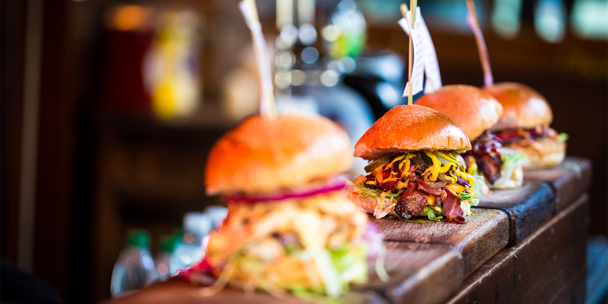 Three hamburgers loaded with various toppings sit on a bar top waiting to be taken out to diners 