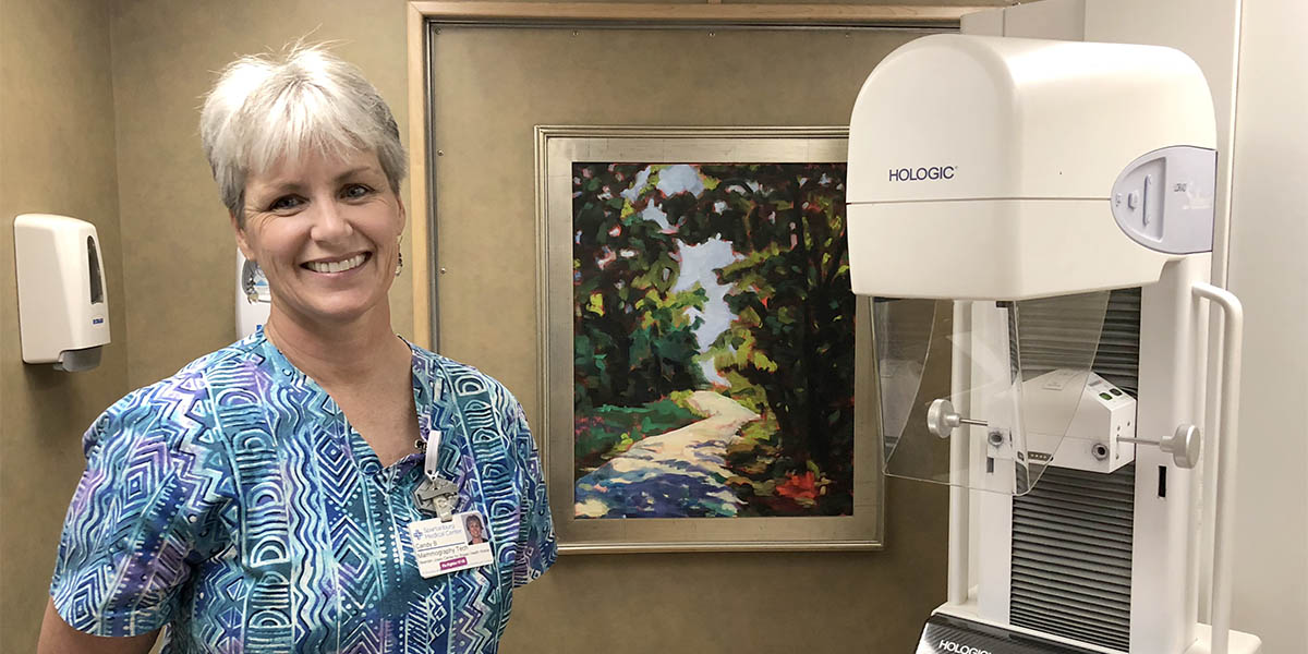 A mammography technician stands in front of a hologic machine