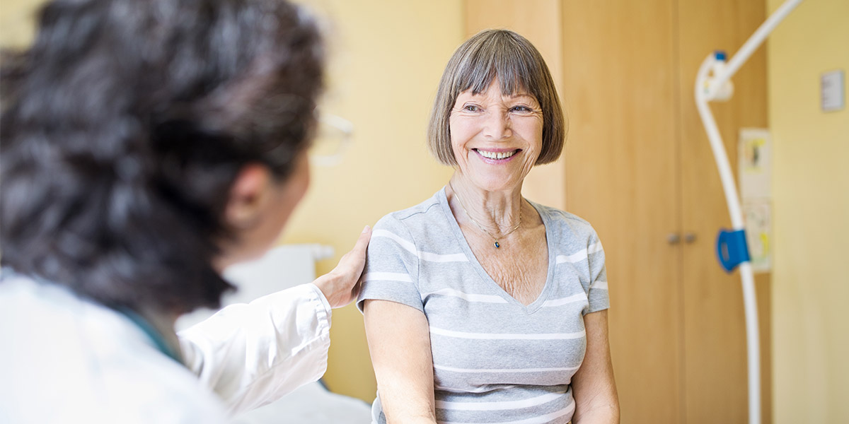 An elderly female patient smiles at a doctor