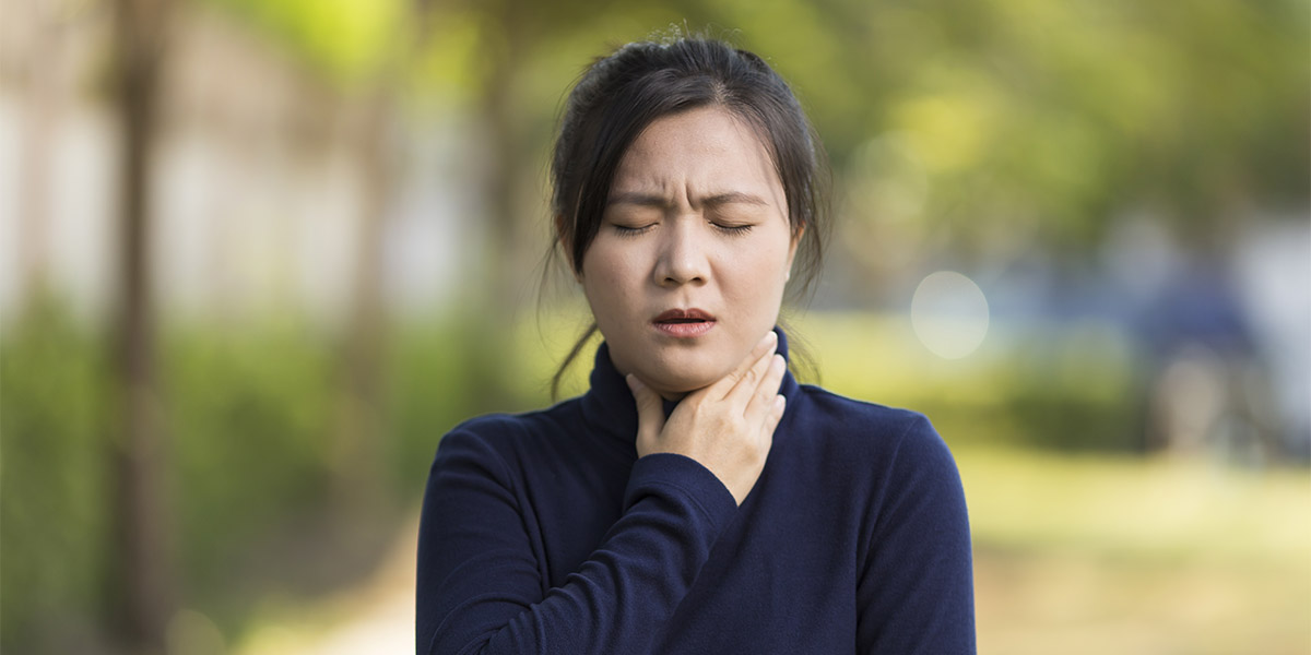 A woman having an allergic reaction is holding her throat with a pained expression on her face