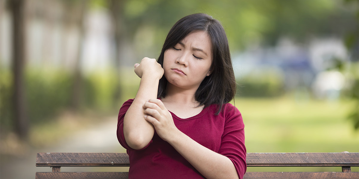 Woman Scratching Her Arm Sitting on Bench at Park