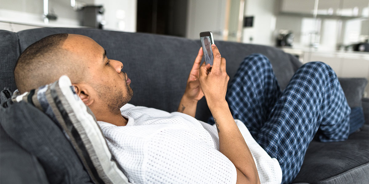 A man laying on his couch and using his smartphone for a telehealth virtual visit
