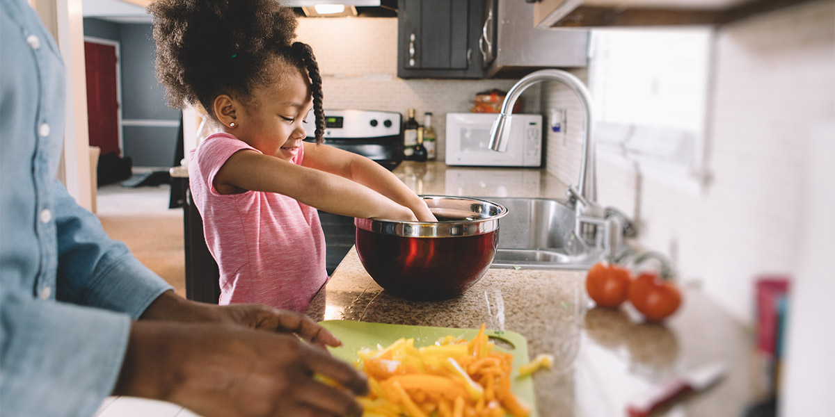 Young girl prepares food in a bowl beside her mother