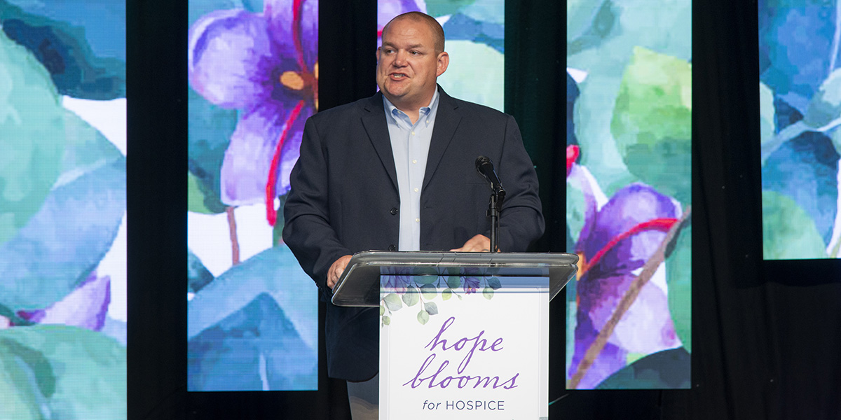 Reid Bowyer speaks on stage at the at Hope Blooms for Hospice Luncheon