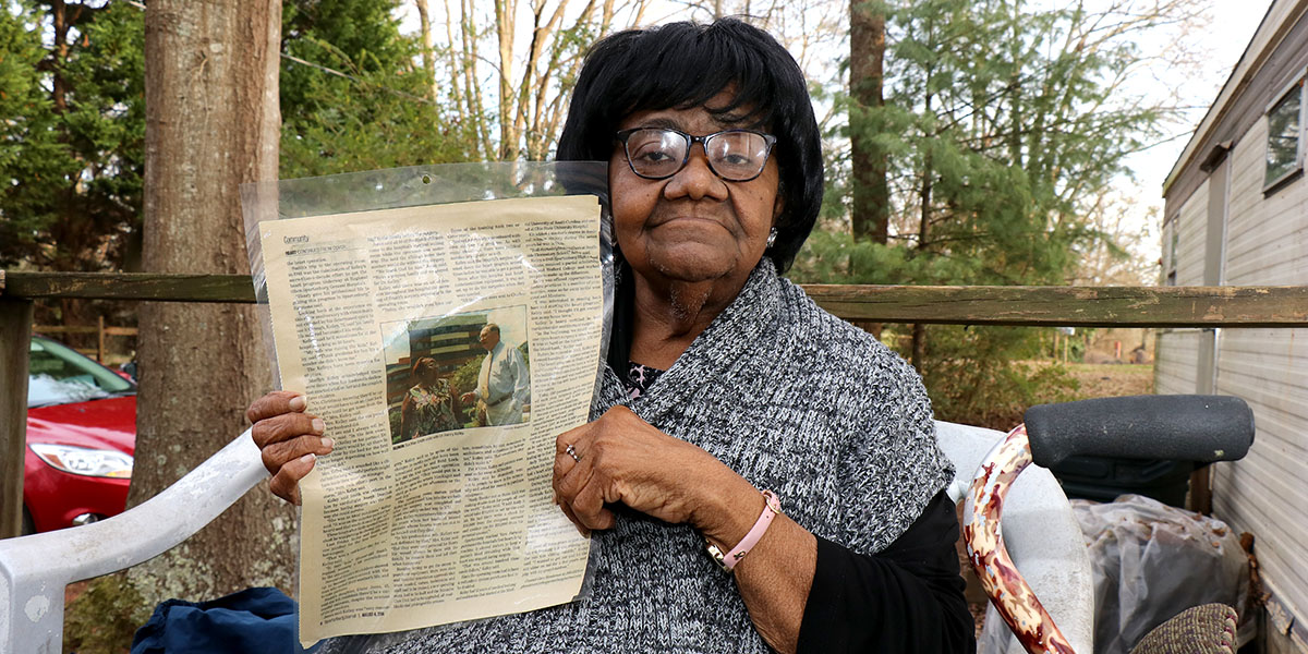 Eva Mae Smith holding an old newspaper article that reports her being the first open-heart surgery patient at Spartanburg General Hospital, the former name of Spartanburg Medical Center.
