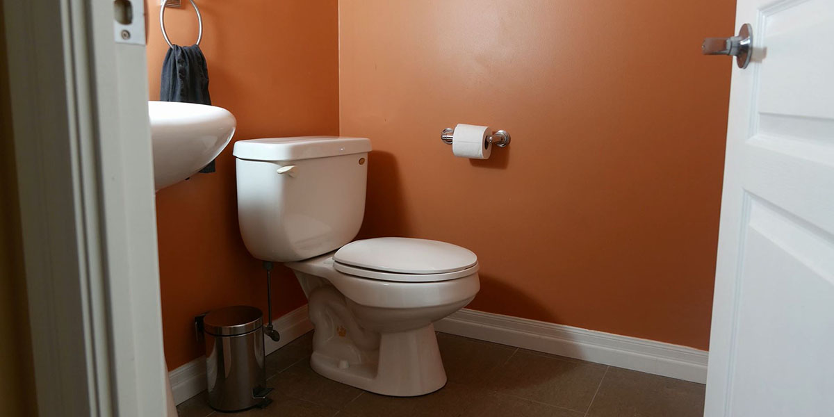 A toilet and sink from the entry way of an orange half bathroom