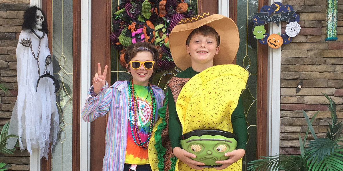 Two children pose in their Halloween costumes in front of a door