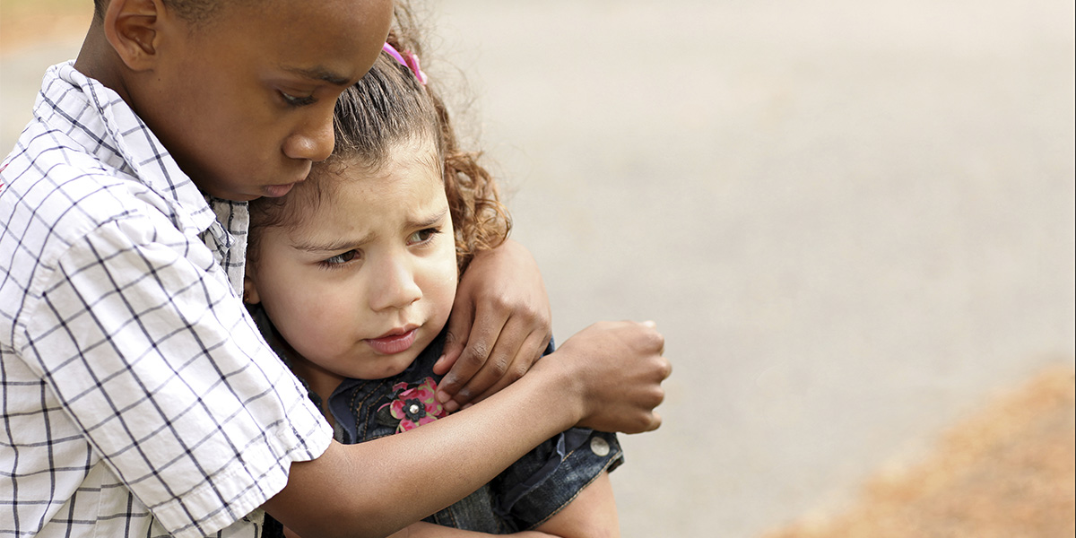 A young girl being bullied is being comforted by a friend