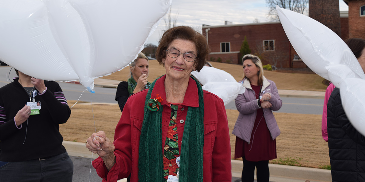 Inez Golden stands in front of a group holding a white balloon at the Light Up a Life bereavement event