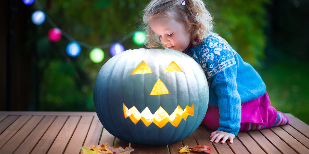 A little girl looks at the inside of a teal jack-o-lantern