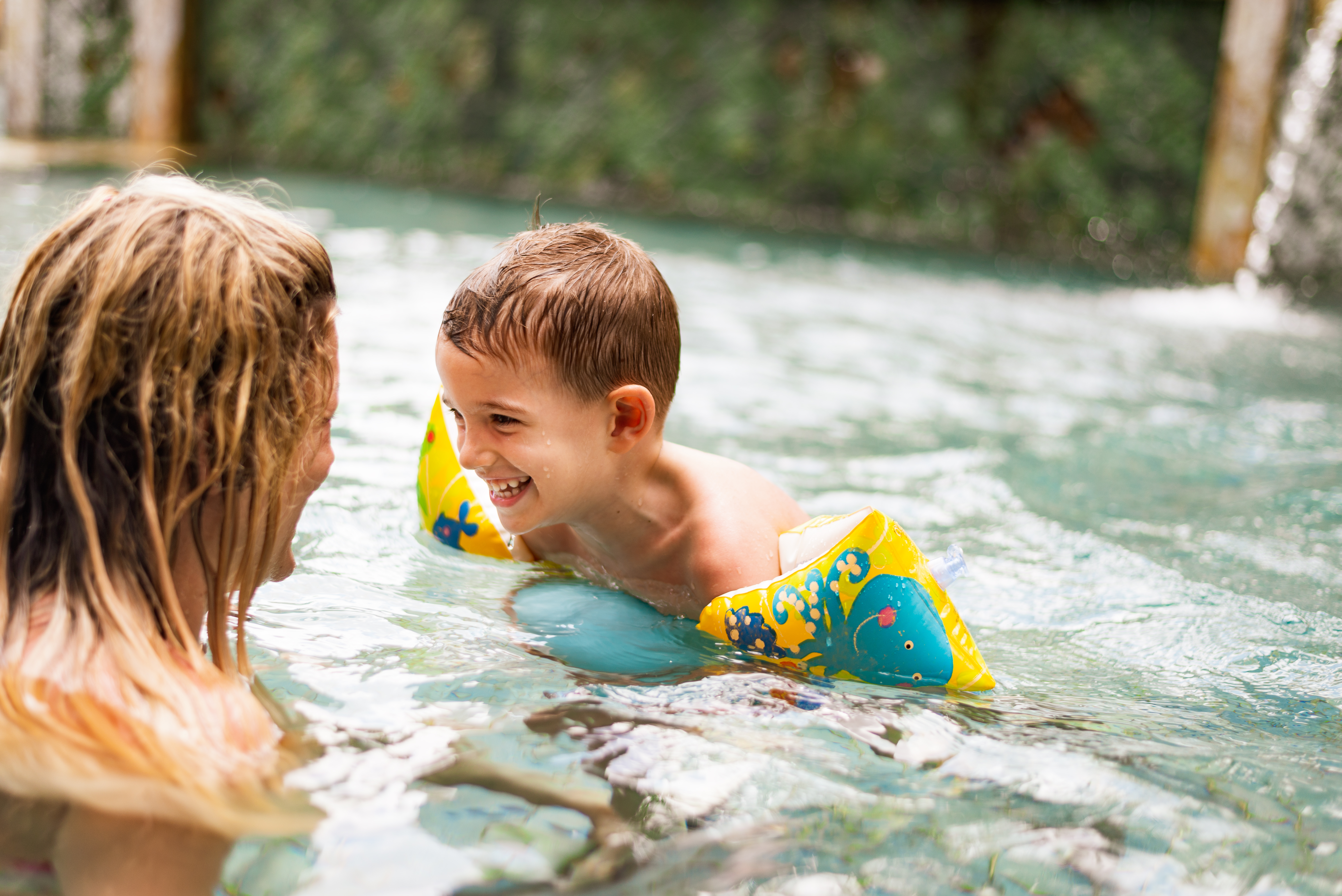 Happy little boy having fun in the swimming pool with his mother