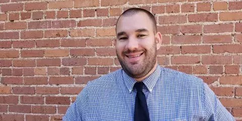 Bradley Horne, DO pictured smiling in front of a brick wall switched career paths to become a phycician after his mother was diagnosed with cancer.jpg