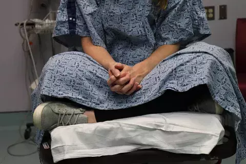The lower half of an unidentifiable patient is shown wearing a hospital gown and sitting on a table in a hospital room waiting to be examined by a sexual assault nurse examiner (sane).jpg
